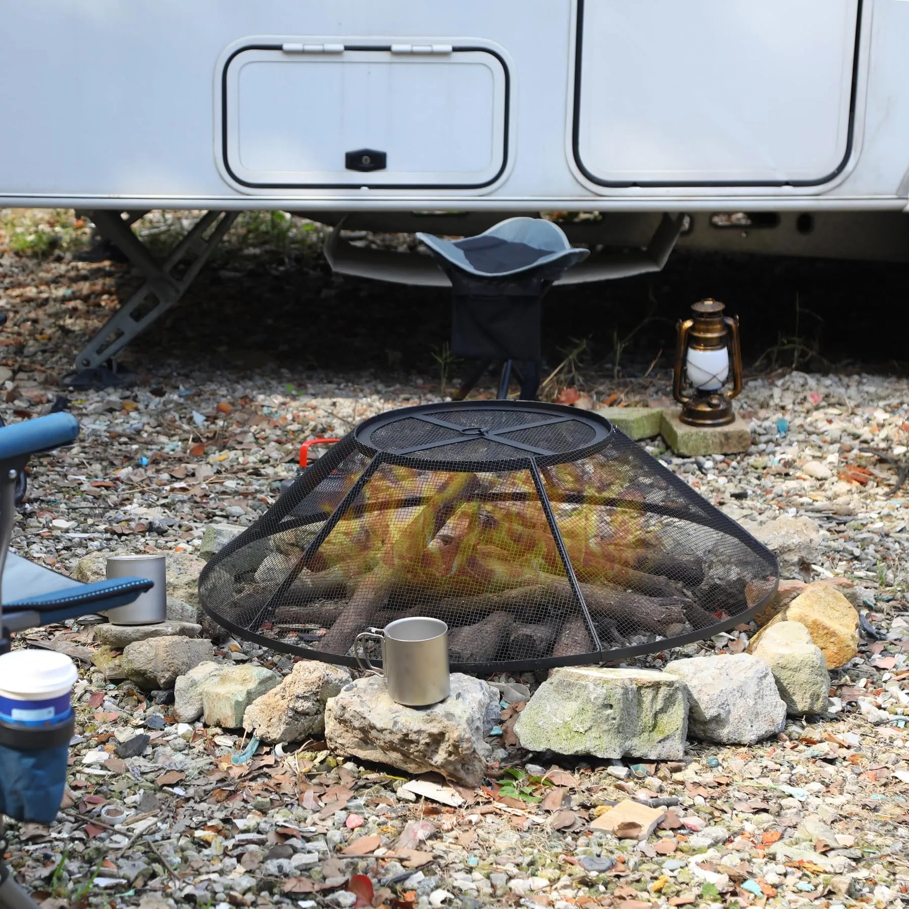 Fire pit with flames in front of a trailer on a gravel surface